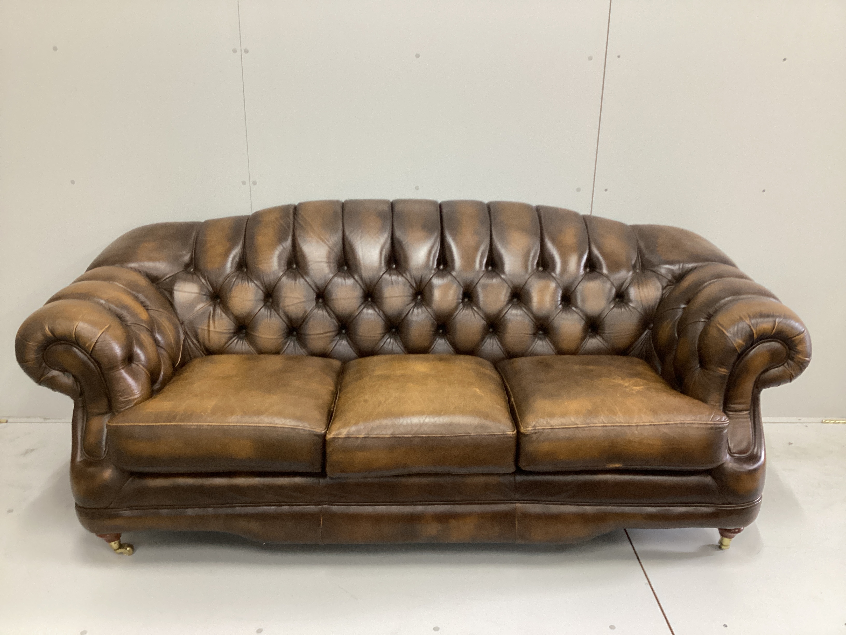 A Thomas Lloyd buttoned brown leather three seater settee, a two seater settee and a footstool, largest length 216cm, depth 90cm, height 85cm